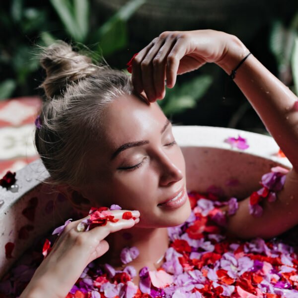Close up photo attractive tanned woman chilling bath full rose petals indoor overhead shot refined blonde female model enjoying spa with gently smile 600x600