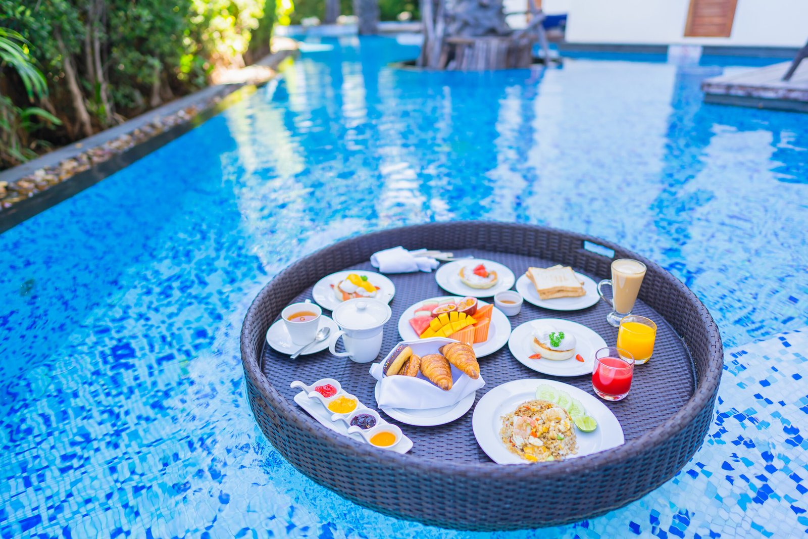 Floating breakfast set in tray with fried egg omelette sausage ham bread fruit milk juice coffee and other around swimming pool