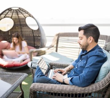 Handsome young latin man sitting armchair using laptop with female colleague background 360x320