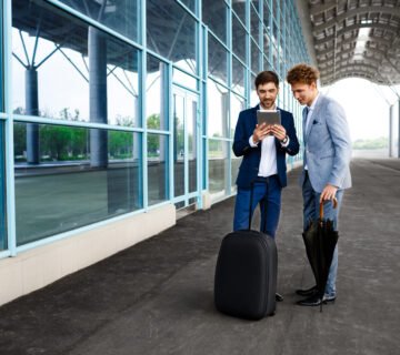 Picture two young businessmen talking rainy station holding tablet 360x320