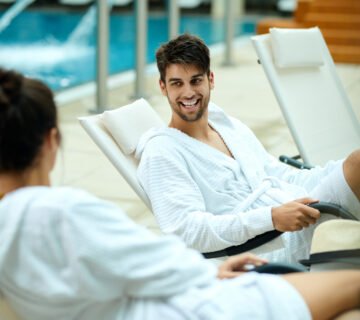 Young couple bathrobes talking while sitting by pool spending weekend spa focus is happy man 360x320